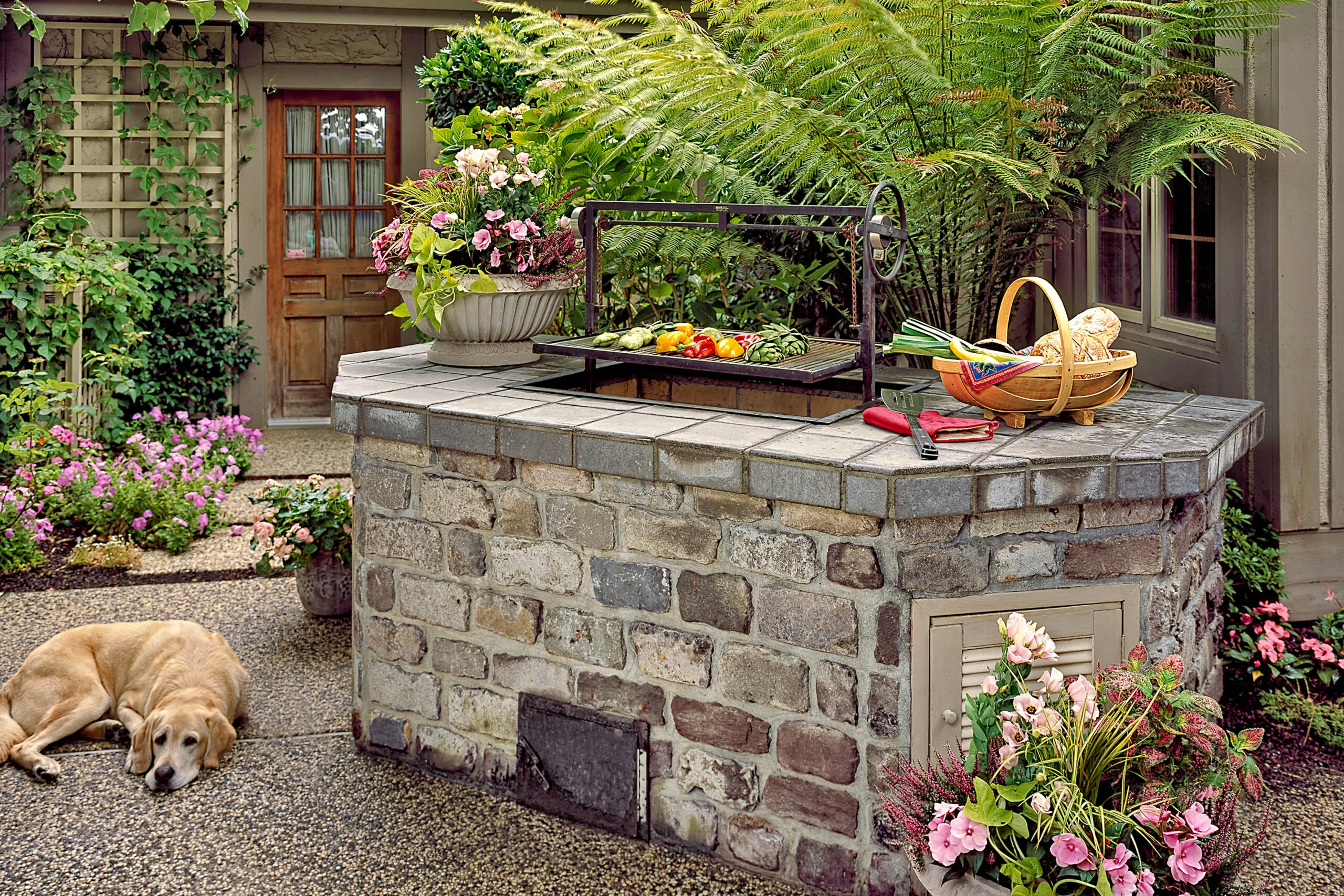A dog lying down next to a stone barbecue pit with vegetables on top of it.