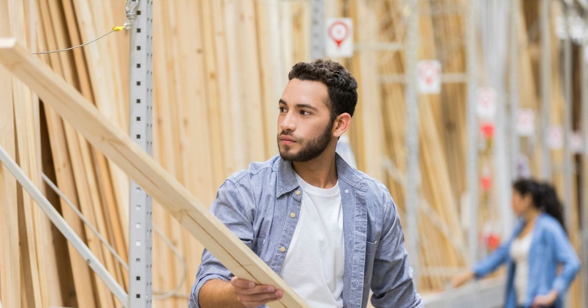 A man at a lumber store looking at a board of wood.