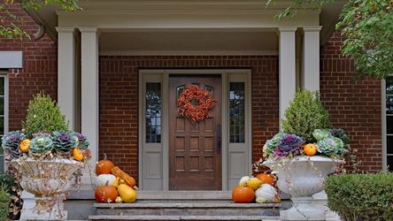 Front entrance of a home with pumpkins decorating the steps and an autumn wreath hanging from the front door. Lead image for best fall decor ideas.