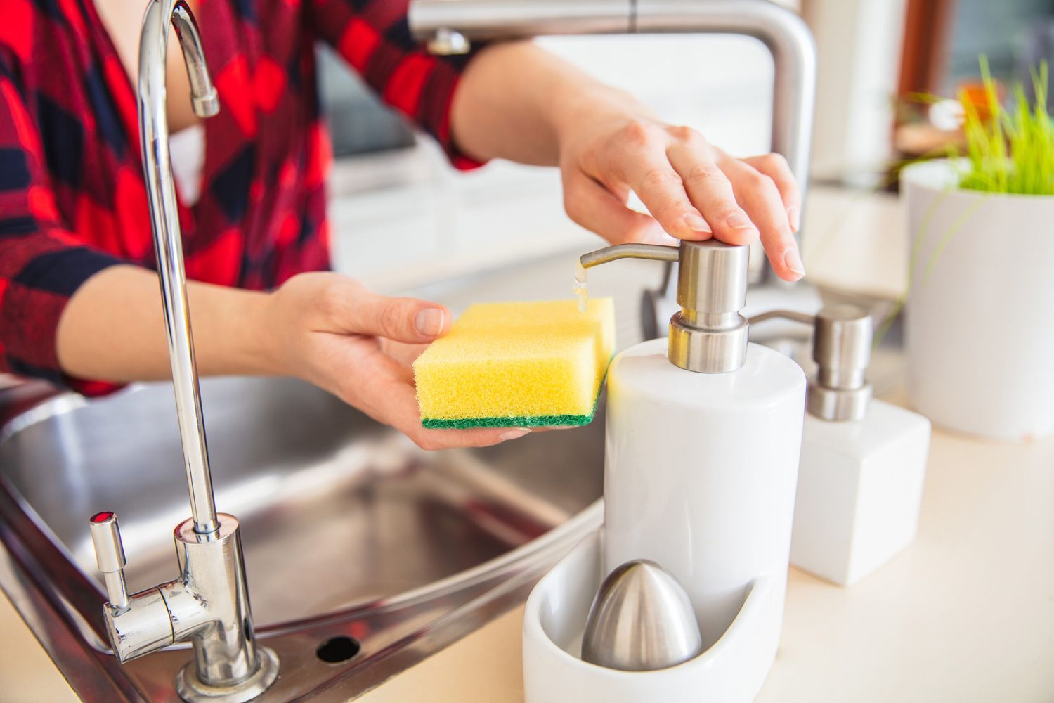 A person dispenses dish soap onto a clean kitchen sponge.