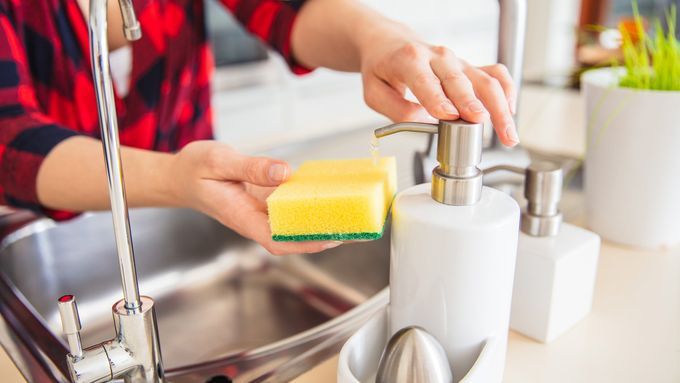 A person dispenses dish soap onto a clean kitchen sponge.