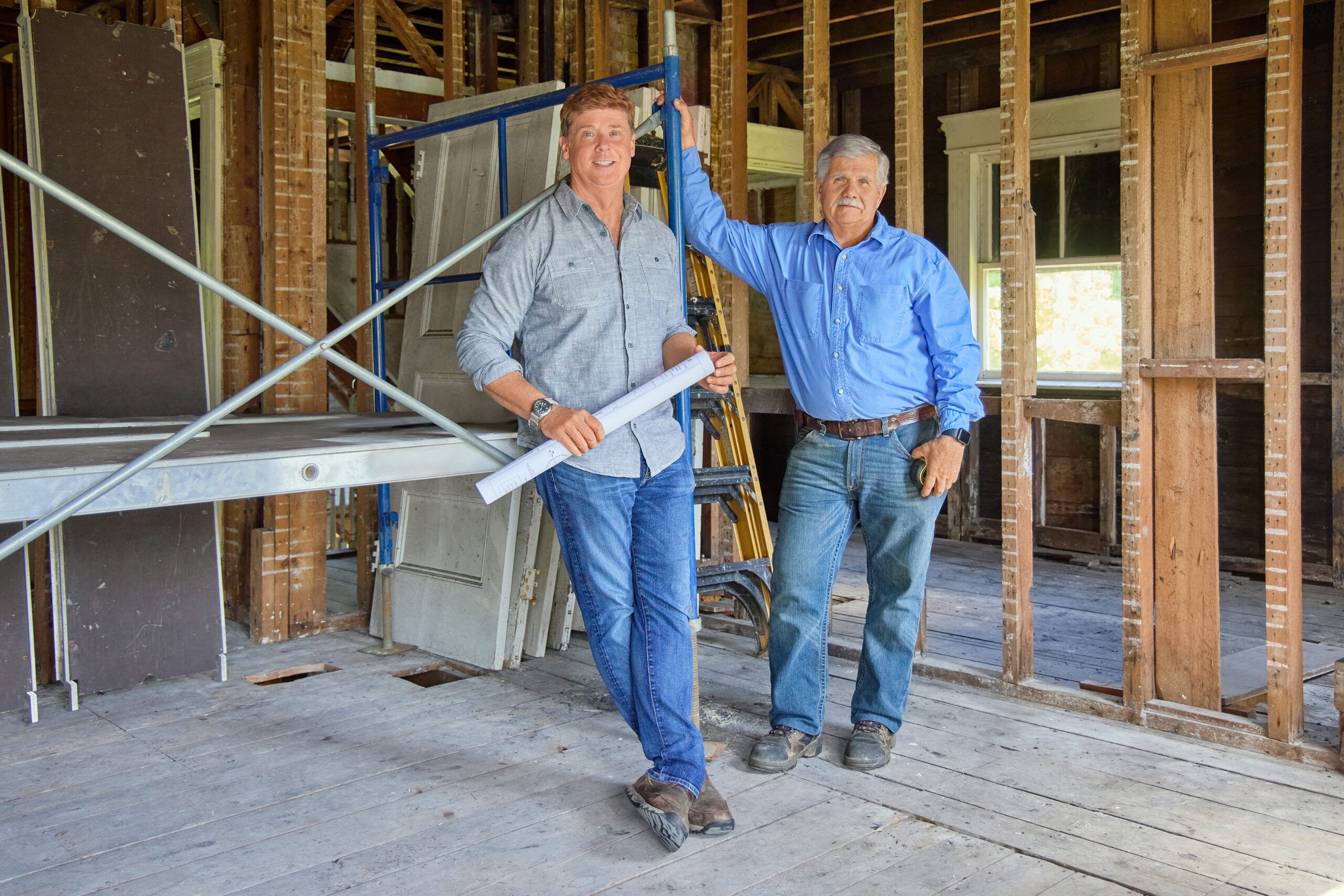 Tom Silva and Kevin O'Connor leaning on scaffolding in an empty house