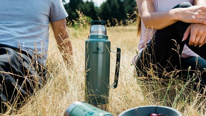 Stanley Coffee mug in between two people in a grassy field. Lead image for 5 Best Coffee Thermoses review and guide