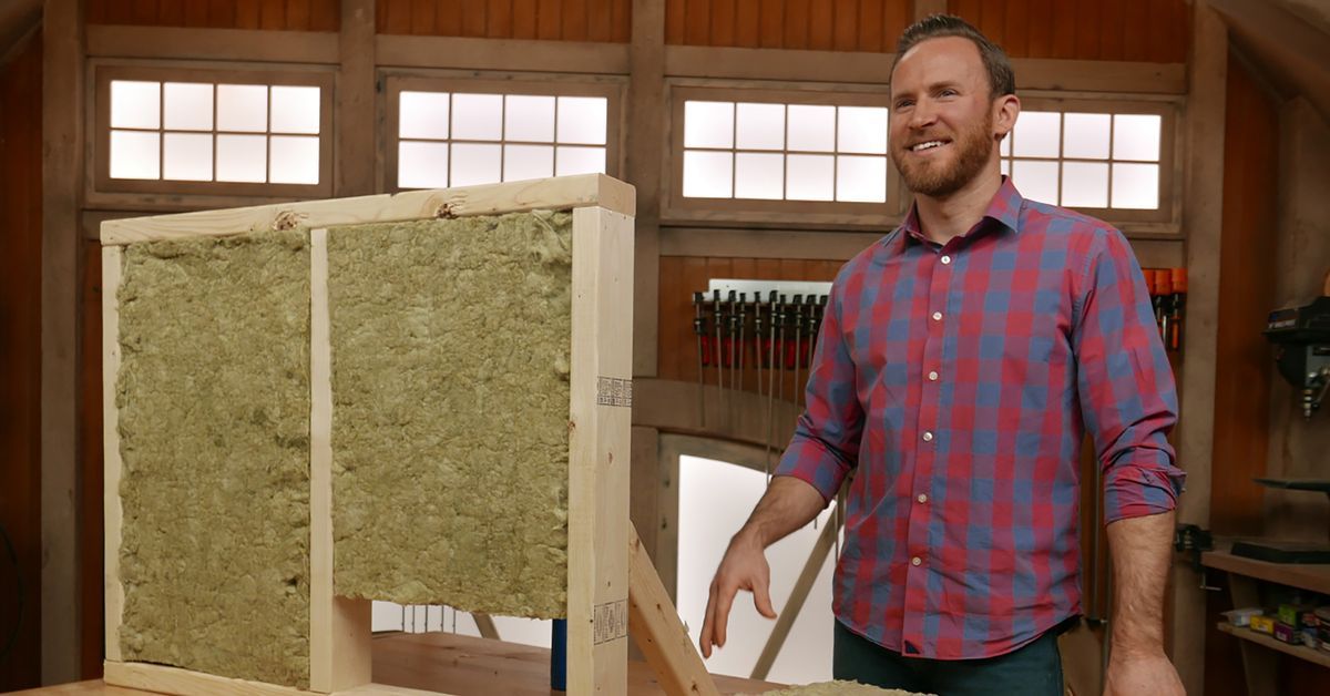 A man standing beside a wooden frame filled with stone wool insulation material to demonstrate its benefits.