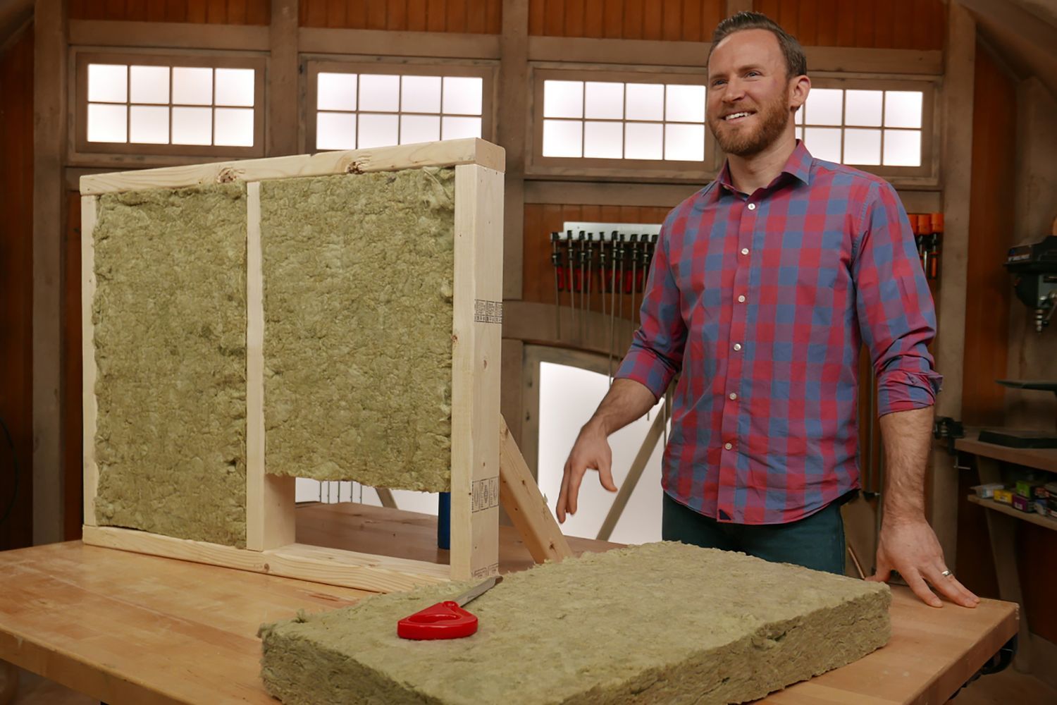 A man standing beside a wooden frame filled with stone wool insulation material to demonstrate its benefits.