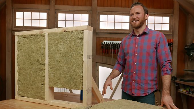 A man standing beside a wooden frame filled with stone wool insulation material to demonstrate its benefits.