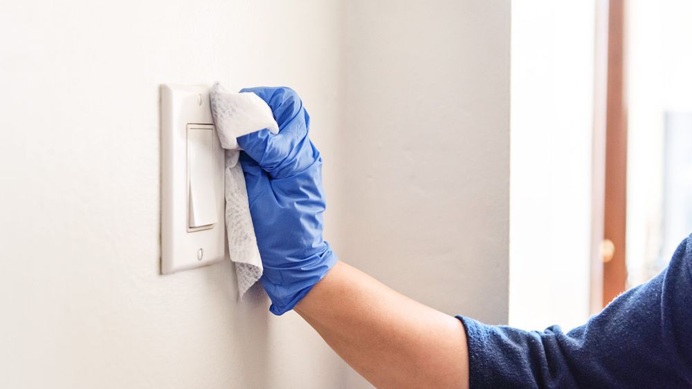 Cleaning a light switch with gloves and a damp cloth.