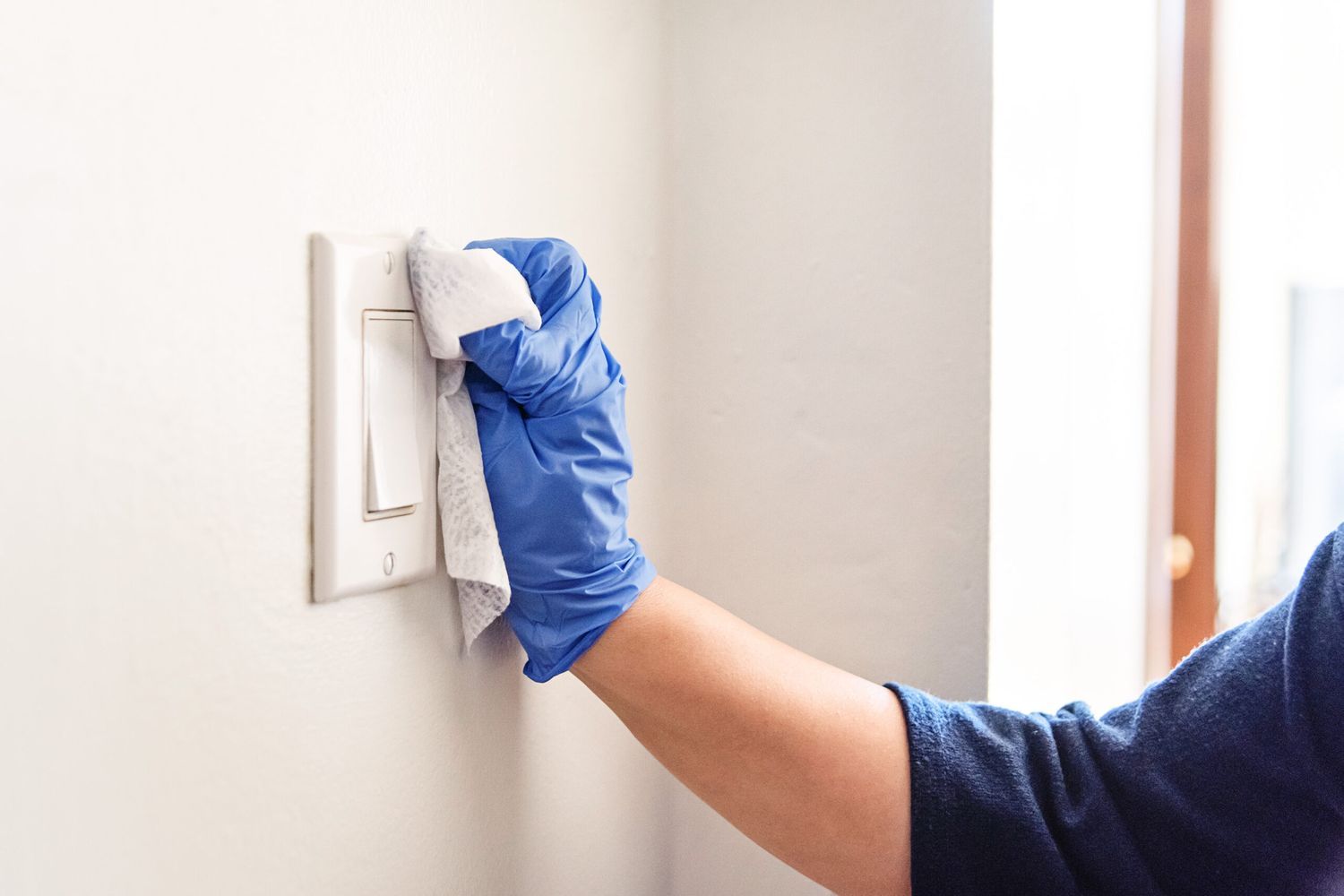 Cleaning a light switch with gloves and a damp cloth.