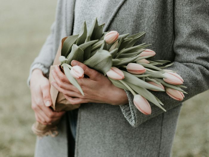 Close-up of a woman's hands holding a bouquet of light pink tulips against her light gray sweater.
