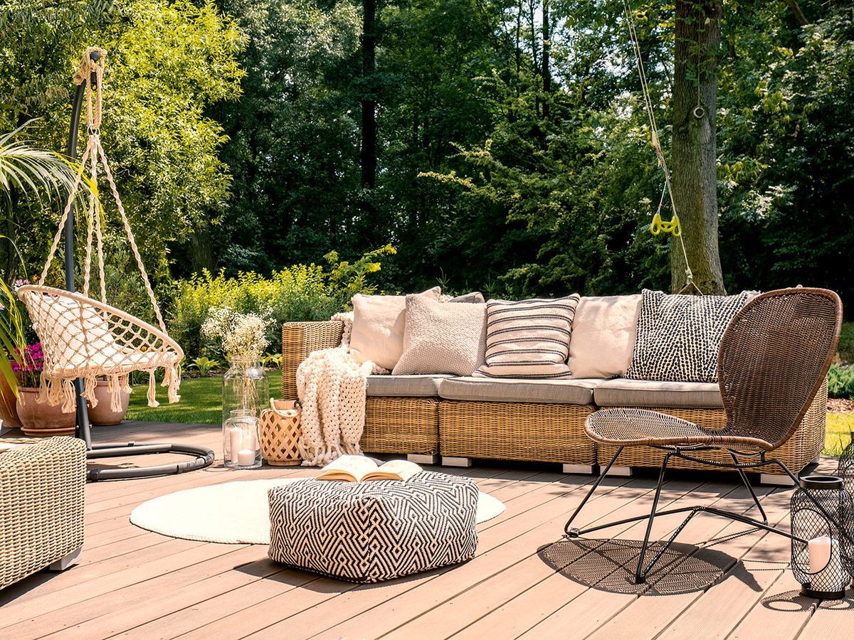 Pouf and rattan chair on wooden patio with settee in the garden during summer.