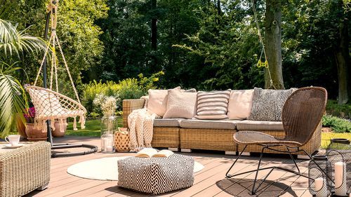 Pouf and rattan chair on wooden patio with settee in the garden during summer.