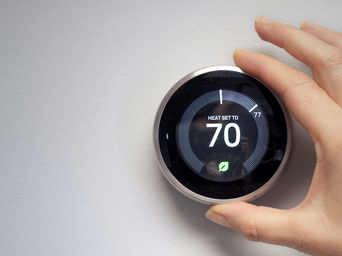 Hand reaches to turn up a smart thermostat.