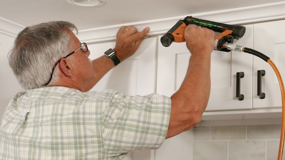 Tom Silva installing crown molding above a kitchen Cabinet.