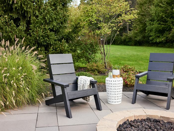 Two modern adirondack chairs painted black in a back yard.