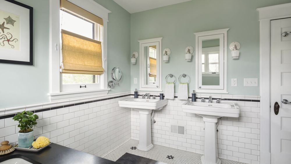 Pretty green and white bathroom with two pedestal sinks seen from tub