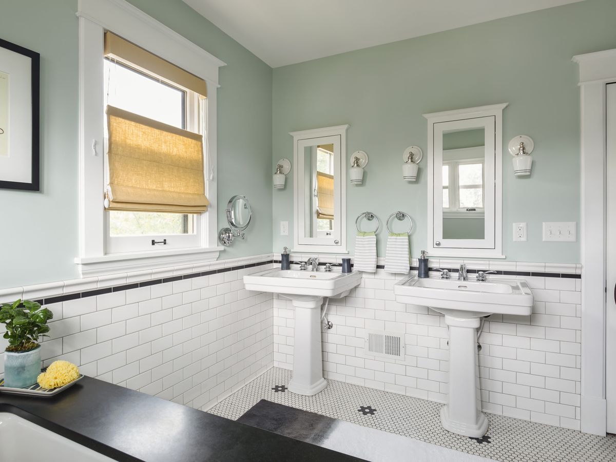 Pretty green and white bathroom with two pedestal sinks seen from tub