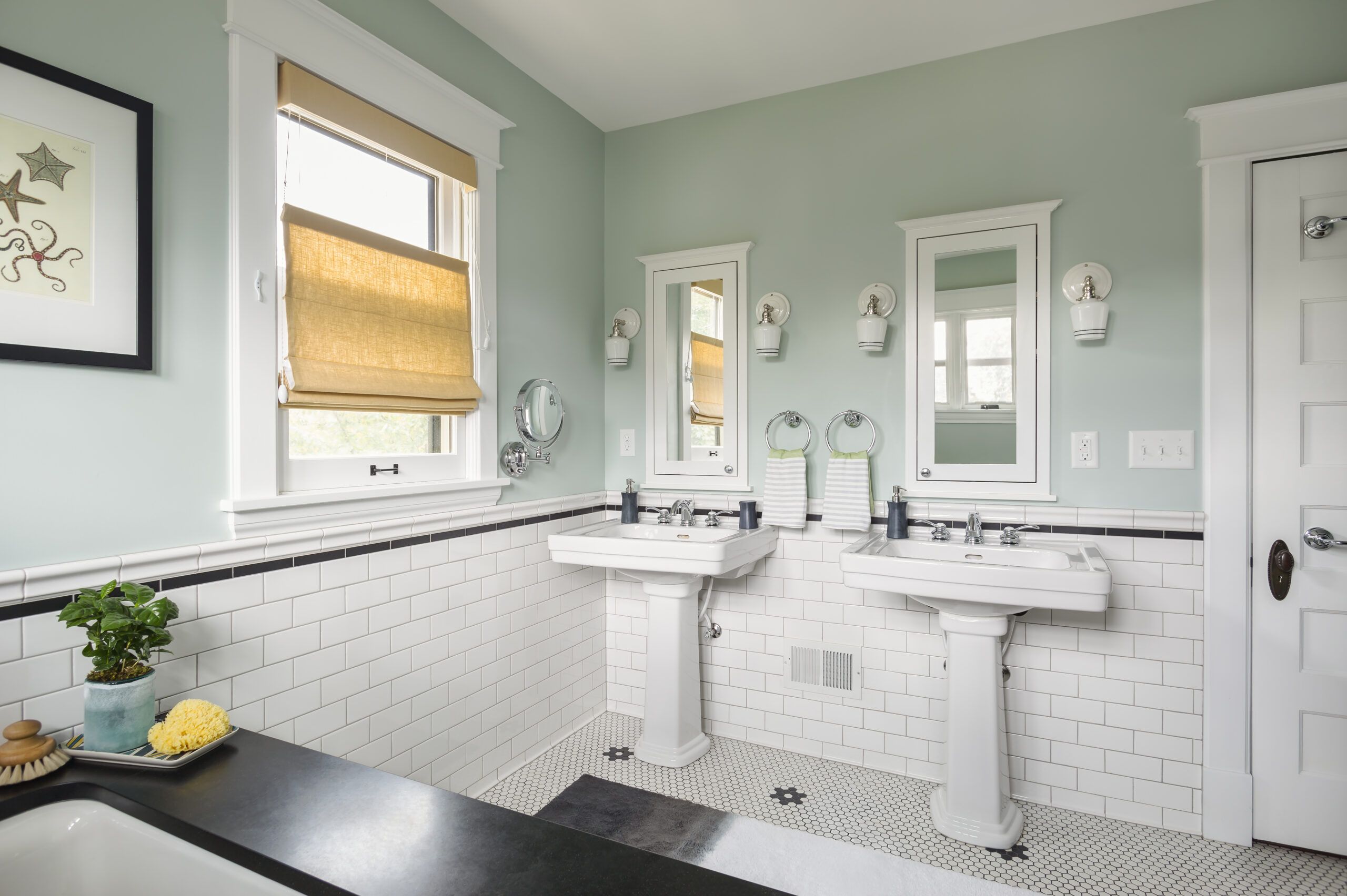 Pretty green and white bathroom with two pedestal sinks seen from tub