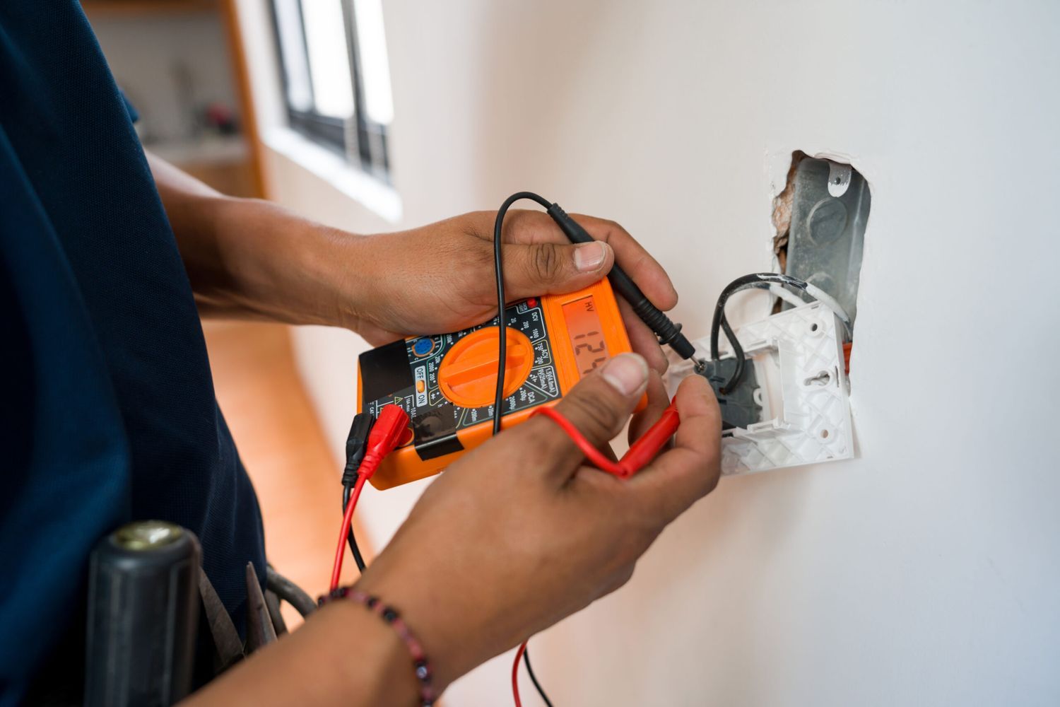 Close-up on an electrician fixing an electrical outlet and measuring the voltage using a multimeter