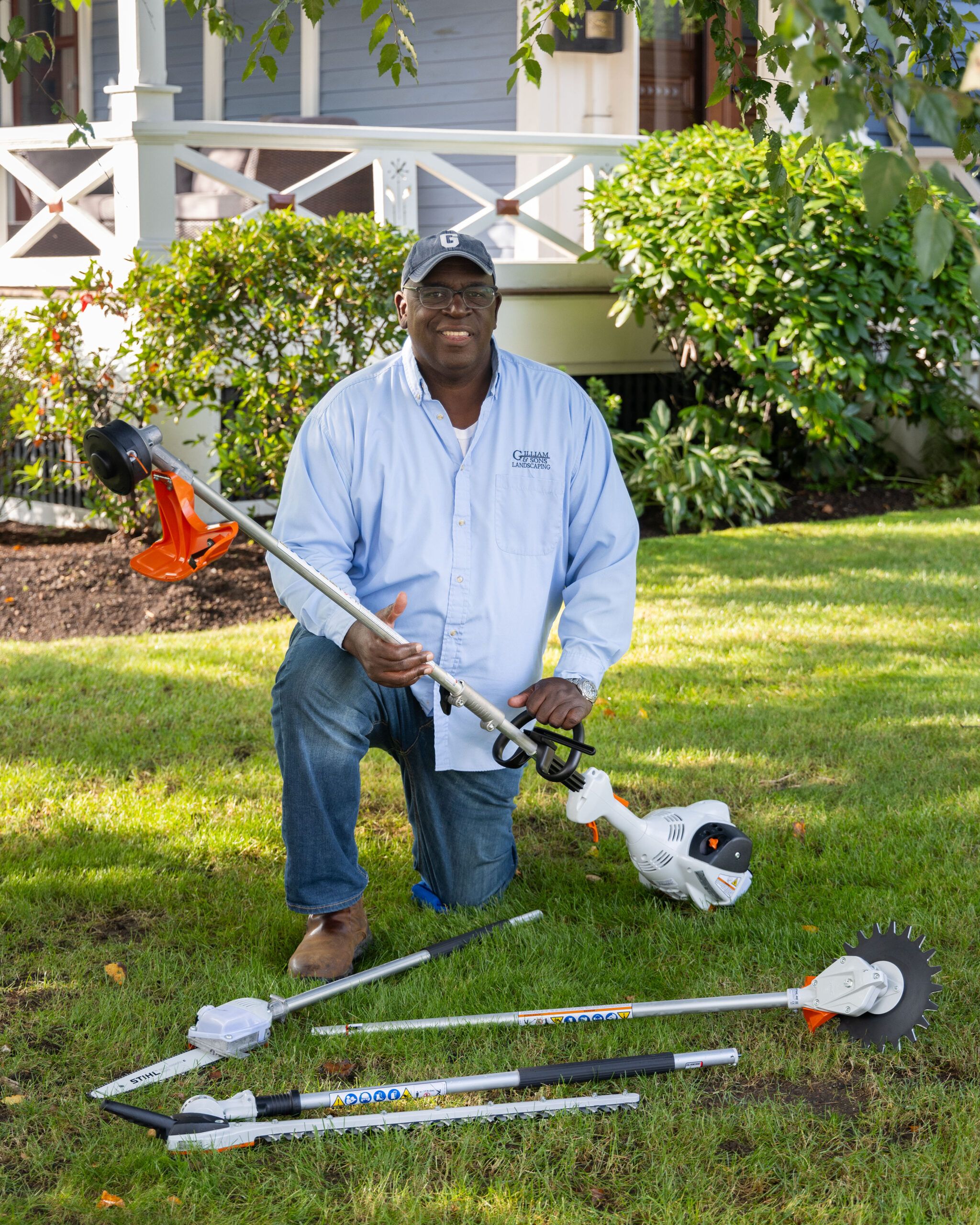 Lee Gilliam holding a multi head trimmer with additional attachments on the ground.