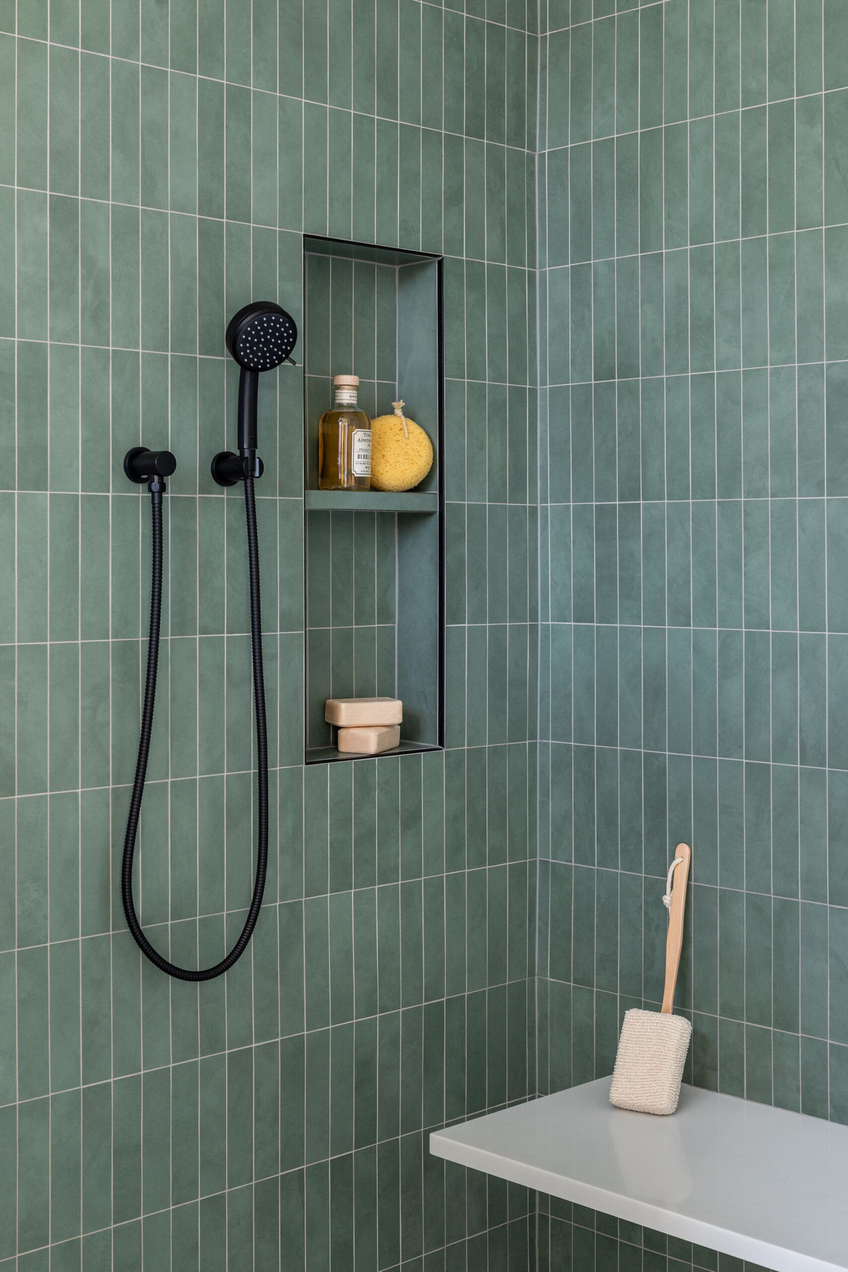 Handheld showerhead in green tiled shower with bench