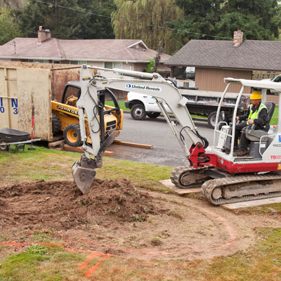 A person operates a small excavator to dig a circular area where the rain garden will go.