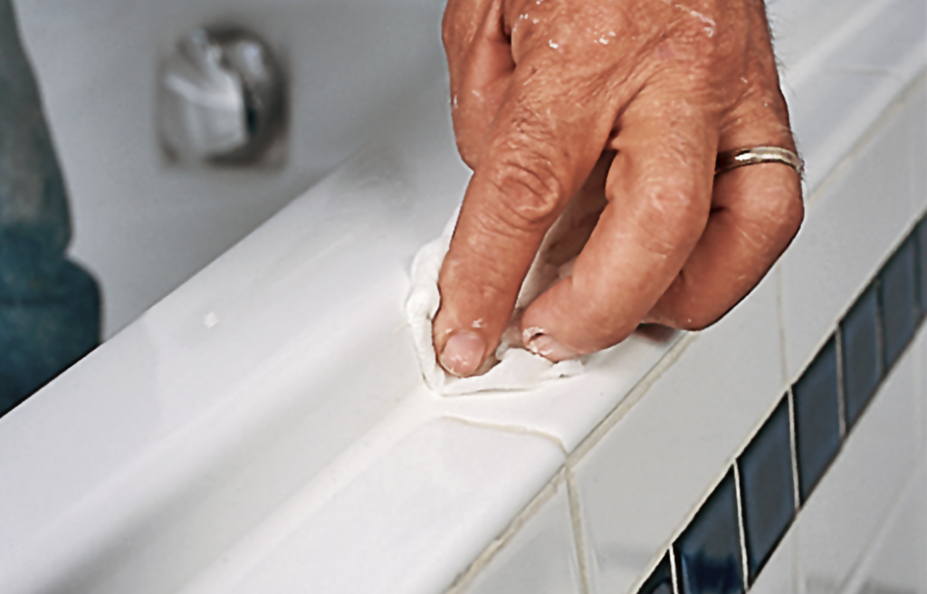 A person smooths the new bathtub caulk.