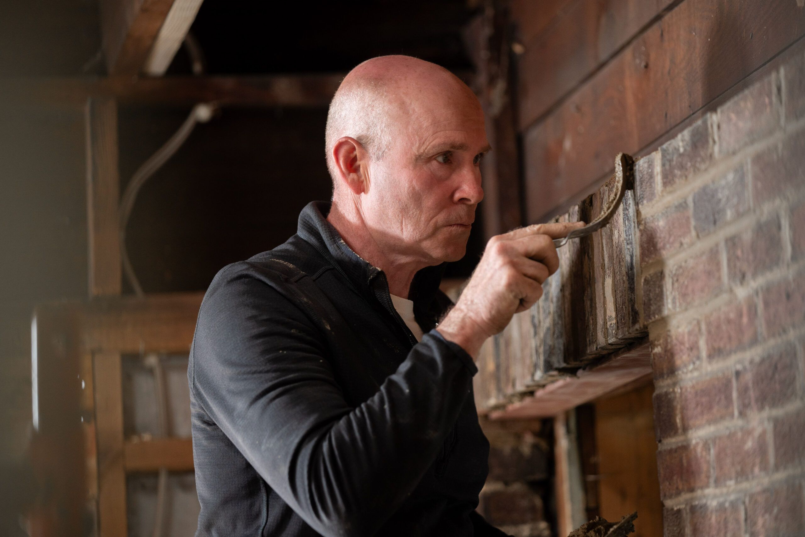 TOH mason Mark McCullough repairs the original brick wall discovered under paneling in a converted porch that will be used as an office.