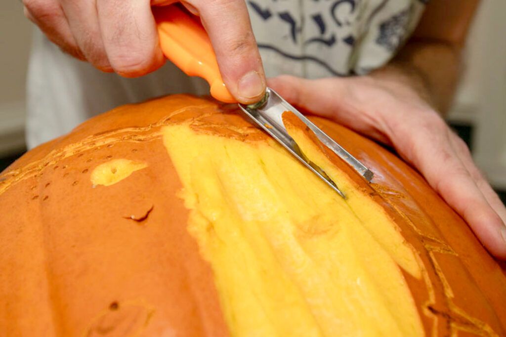 shaving the skin off a pumpkin using a linoleum cutter