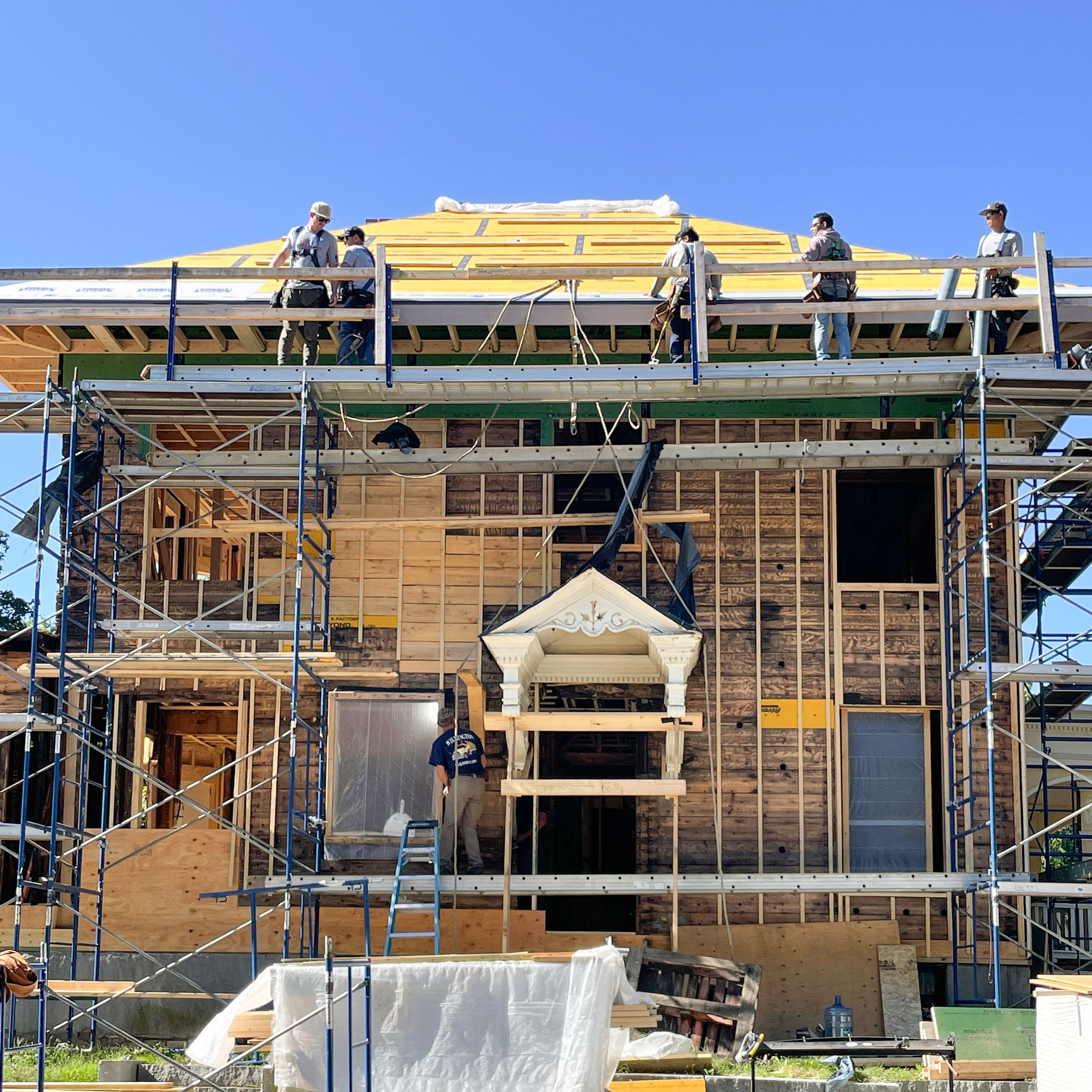 Crews work to protect the roof and sides of the house by adding insulation and weatherproofing membranes.
